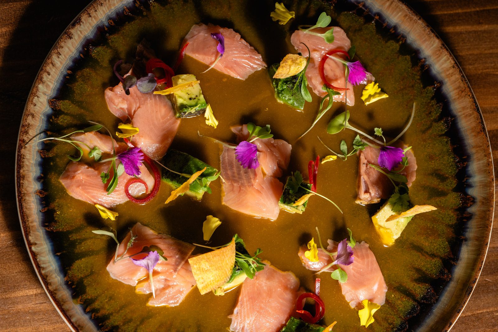 Fine-dining salmon crudo plated with edible flowers and herbs at a Tulum restaurant