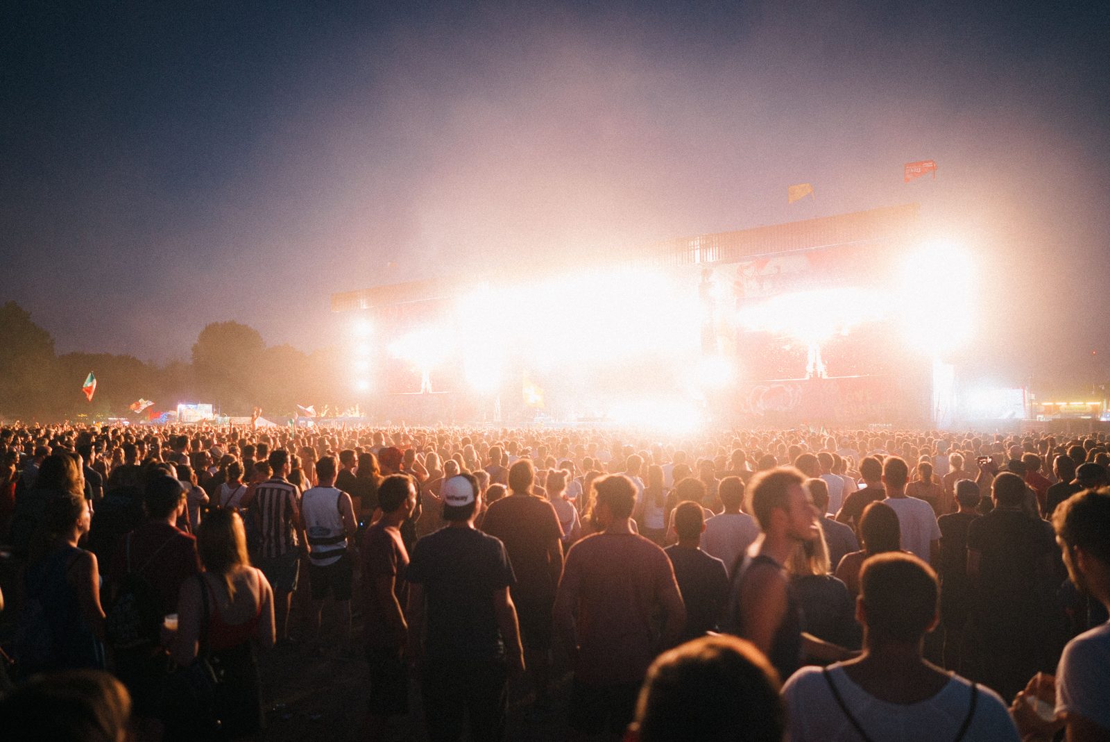 Crowd with hands raised at an outdoor music festival at dusk